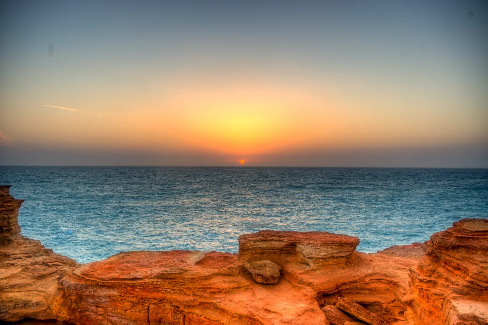 The sun sinking into a turquoise sea behind red sandstone rocks at Gantheaume Point, Broome