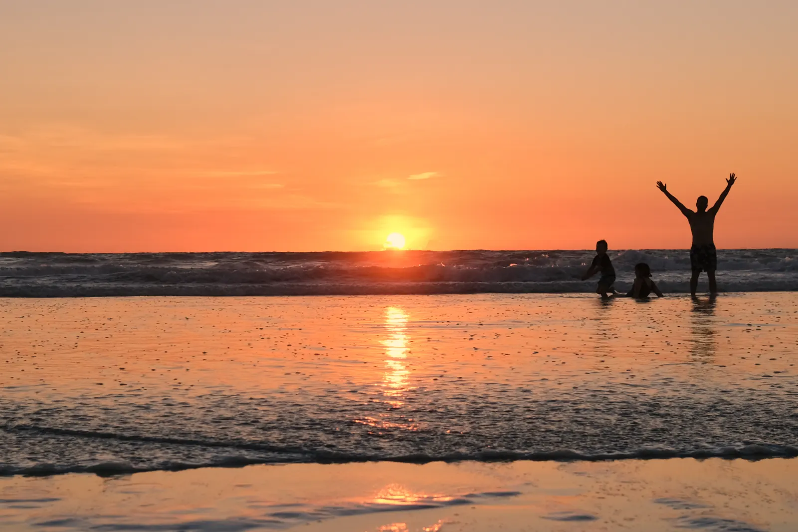 Silhouettes of a swimmer and two children in the shallows of Cable Beach, with the low sun and its reflection on the wet sand